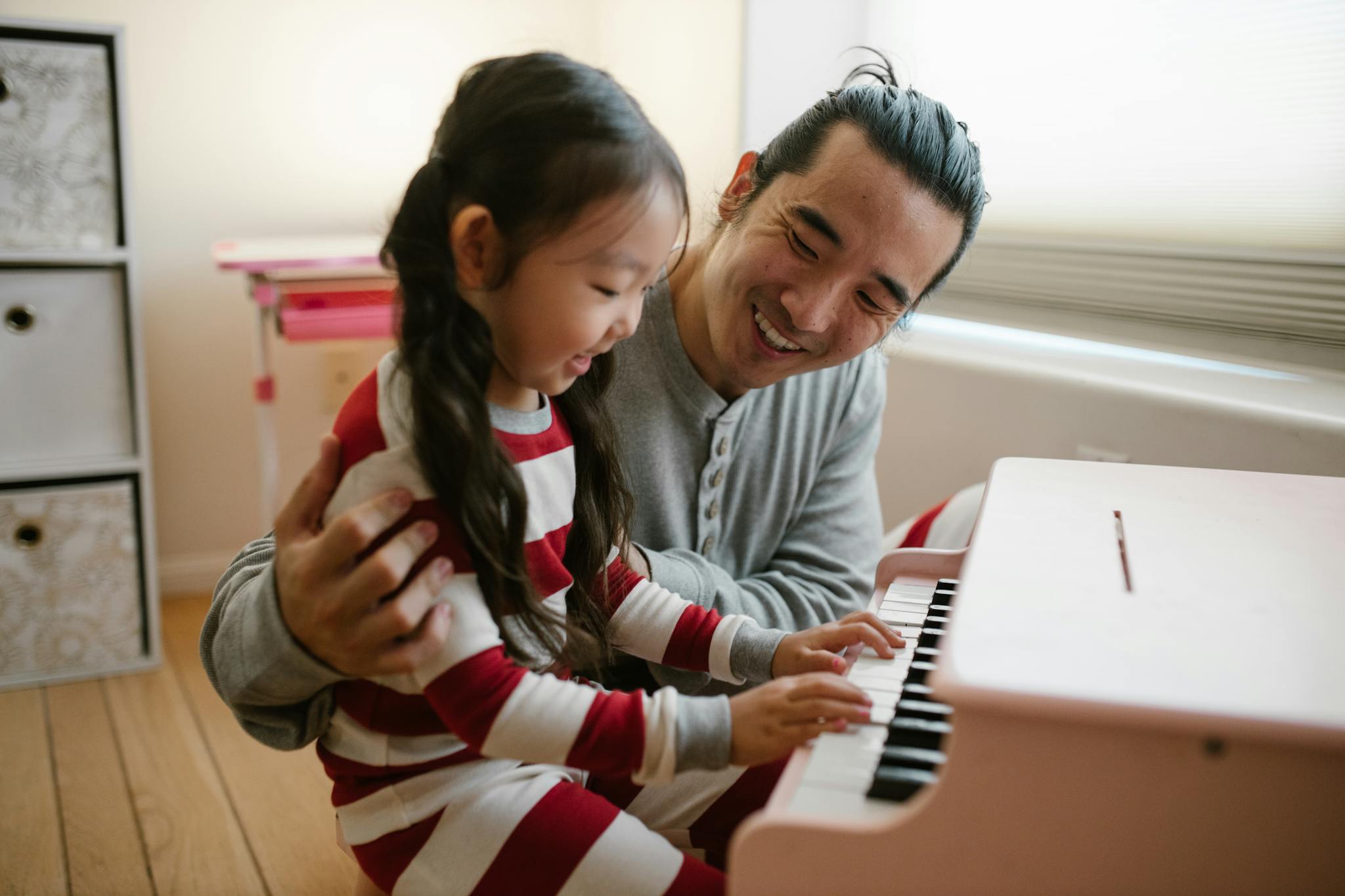 A loving father teaches his daughter to play the piano, creating a joyful family moment.