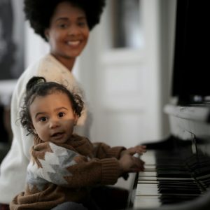 Adorable toddler playing piano with a parent smiling in the background, capturing a warm family moment.